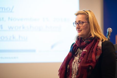 Jela Steinerová hovorí pri mikrofóne, za ňou premietnutá prezentácia.